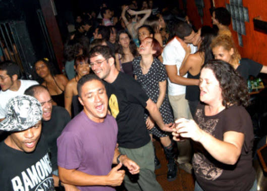Pessoas dançando e cantando numa festa lotada, de roupa casual